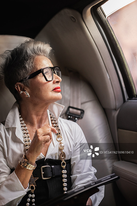 拿着笔和平板电脑望向车窗外的年长女商人图片素材