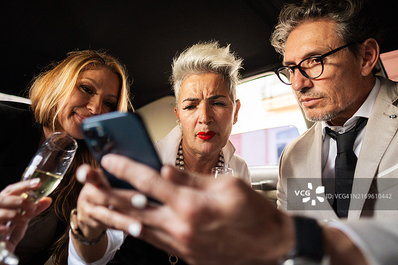 商务人士在豪华轿车内使用智能手机喝香槟图片素材