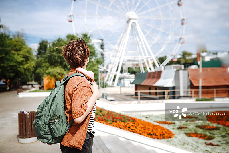少女戴着耳机和背包，独自走在公园的摩天轮附近图片素材