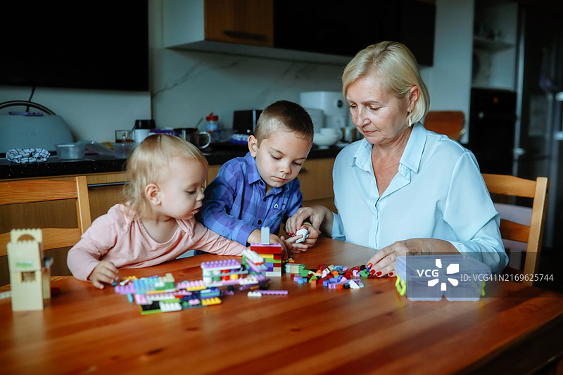 温馨祖孙情：慈祥奶奶与孙辈在厨房玩积木图片素材