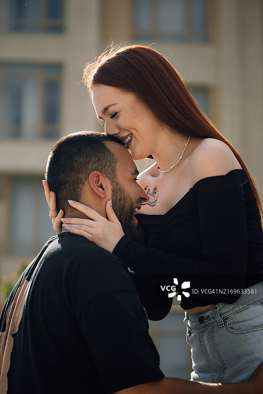 有魅力的红发女人爱抚着英俊的络腮胡伴侣的头，亲吻着他的额头图片素材