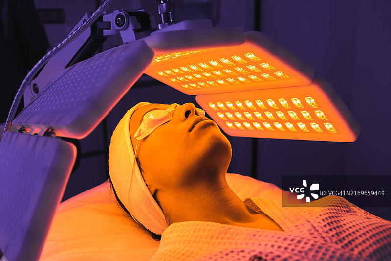 女病人在现代豪华美容诊所接受橙色LED灯或RLT疗法，进行皮肤再生。图片素材