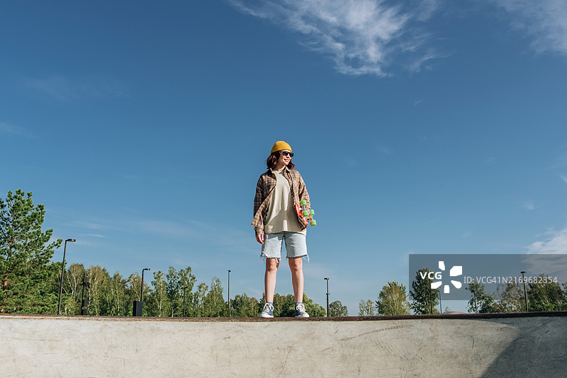 在滑板公园坡道上享受阳光的微笑年轻滑板女孩图片素材