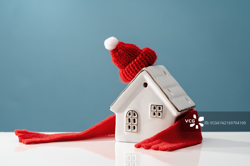 蓝色背景上的白色陶瓷房子与红色针织帽图片素材