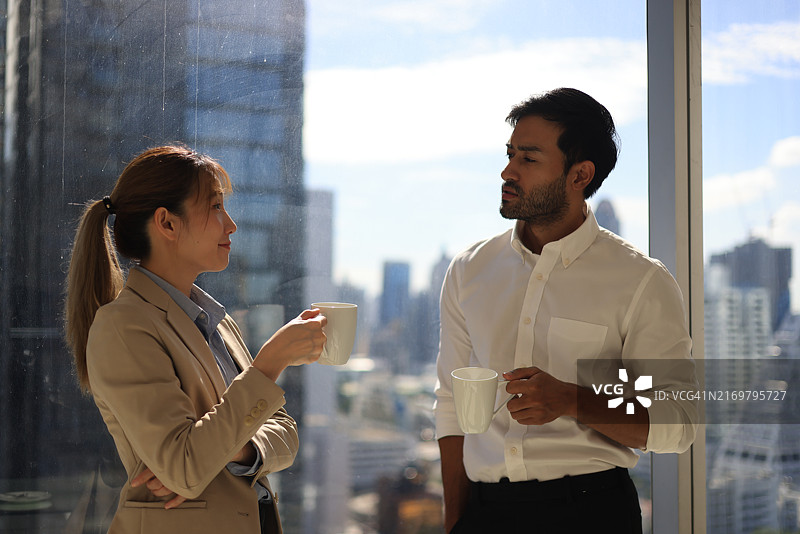 商务人士在休息期间端着咖啡在窗边讨论图片素材