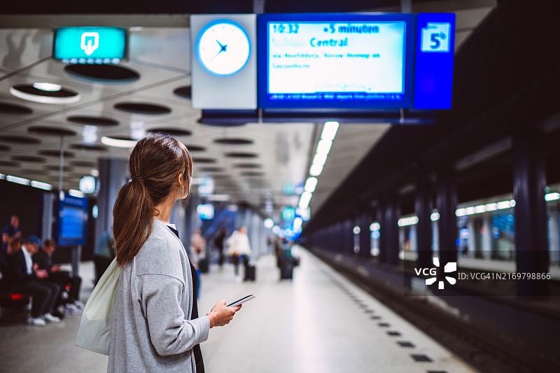 度假期间，女子在火车站台上看列车时刻表的背影图片素材