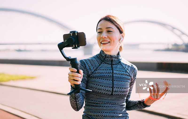 年轻的运动型女性内容创作者使用智能手机在户外录制视频图片素材