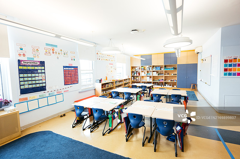 明亮整洁的小学教室，配有蓝色桌椅、书架、教育海报和蓝色地毯图片素材