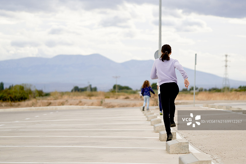 两姐妹穿着休闲装在停车场跑跳，后视图图片素材