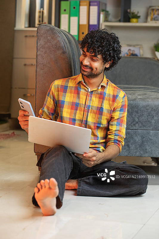在家用智能手机和笔记本电脑工作的年轻男人图片素材