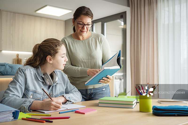 母亲辅导女学生做作业，她们在课本中查找信息图片素材