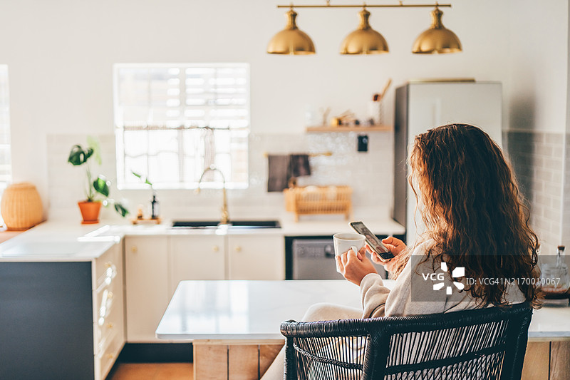 一位女性在家中喝早晨咖啡时查看手机。图片素材
