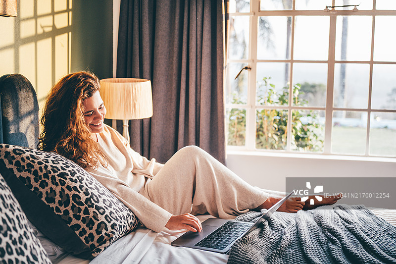 一位女性在床上使用笔记本电脑。图片素材