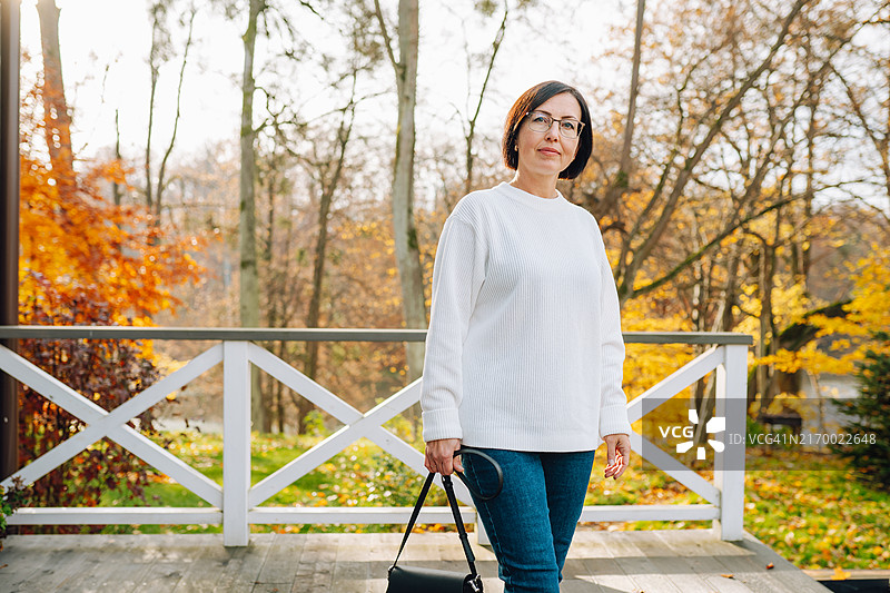 在自然中度过秋季假期，成熟女人在小木屋露台上休息图片素材