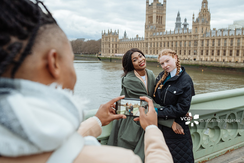 两个不同的女人在伦敦议会大厦前合影，由朋友在威斯敏斯特桥上拍摄图片素材