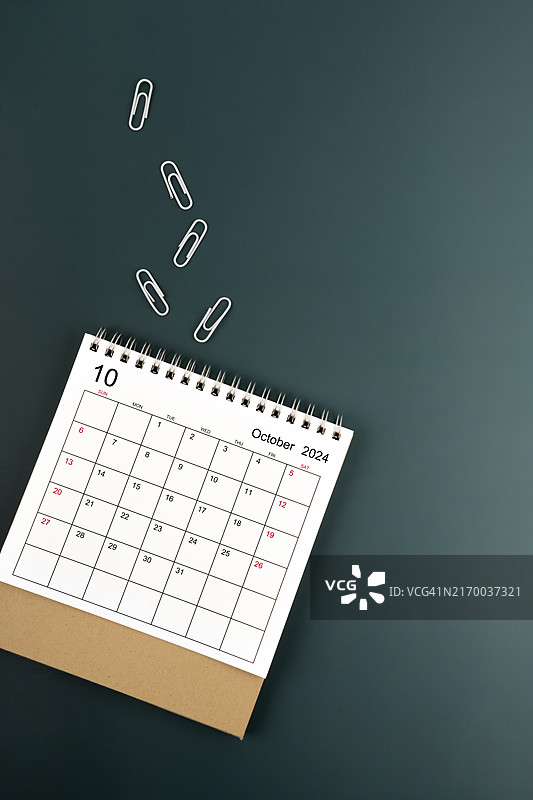 深绿色背景上的2024年10月桌面日历和回形针，带有文案空间图片素材