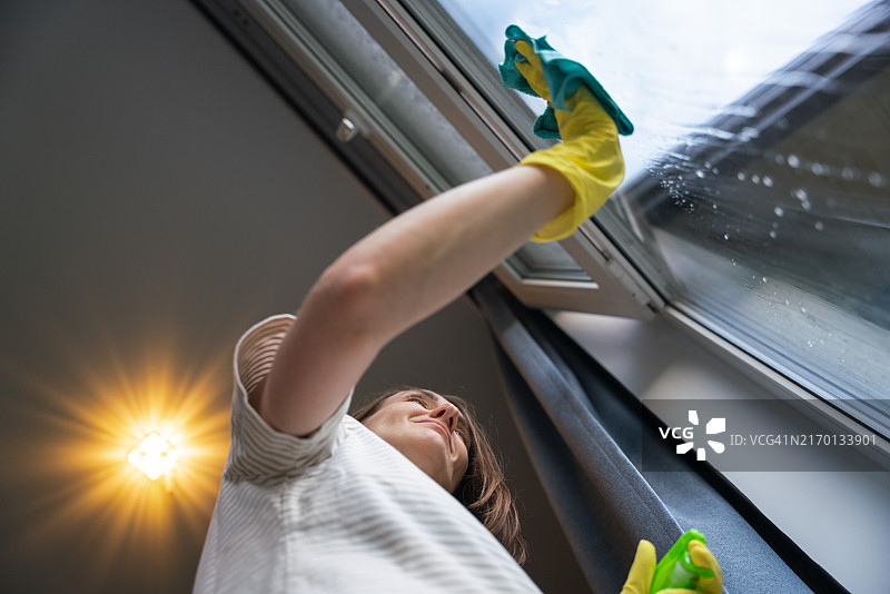 积极的女人在家擦窗户，低角度视角图片素材