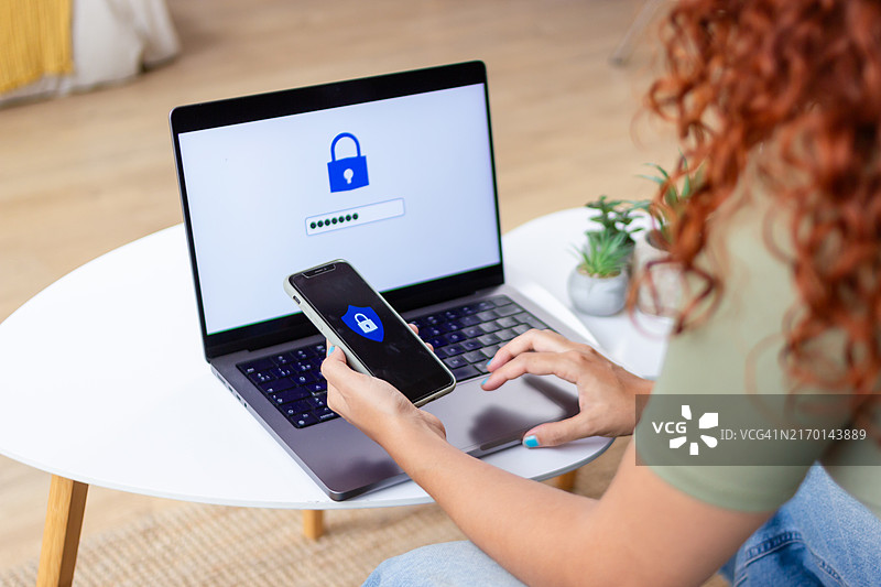 在家中使用笔记本电脑和智能手机进行双重身份验证的女人图片素材