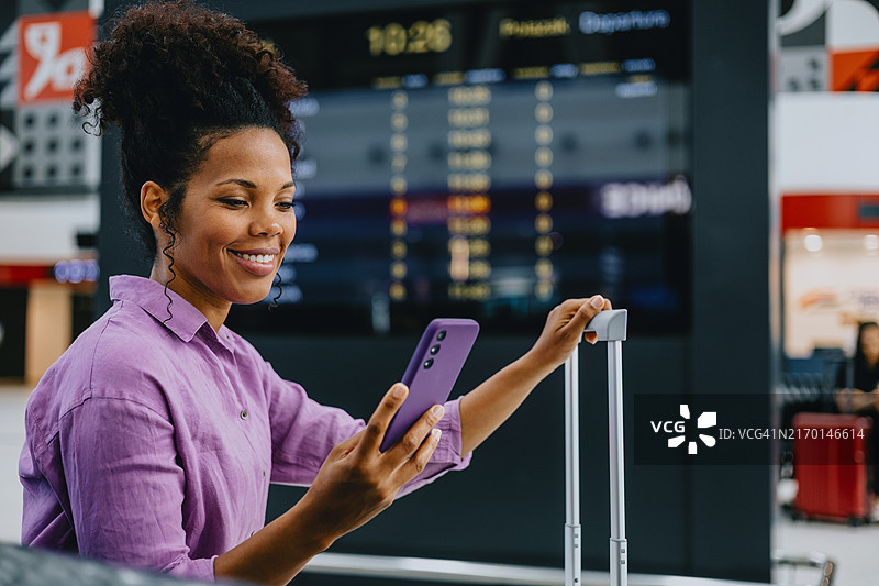 旅客在机场查看手机，背景是航班信息屏幕图片素材