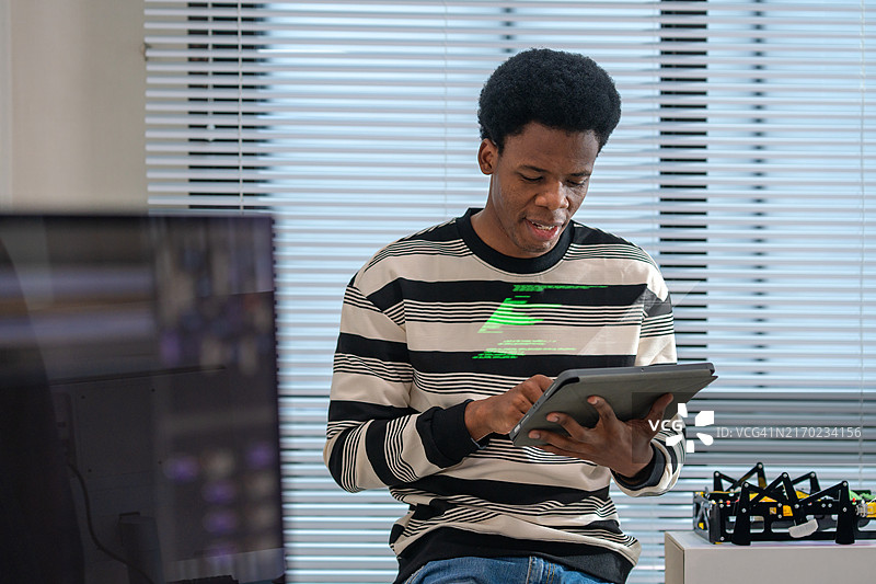 通过机器学习改进自动化工作流程，简化软件开发中的软件测试。一位黑人男性软件开发人员在他的科技办公室的办公桌上，在数字平板电脑上编码或调试代码。图片素材