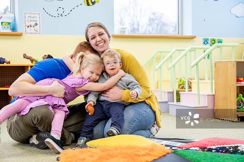 父母和患有唐氏综合征的男孩在日托教室拥抱图片素材
