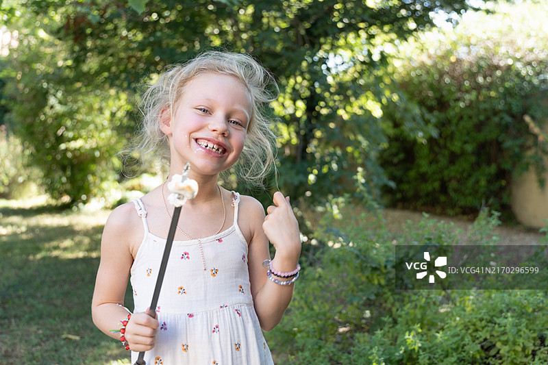 快乐女孩在花园里吃烤棉花糖图片素材