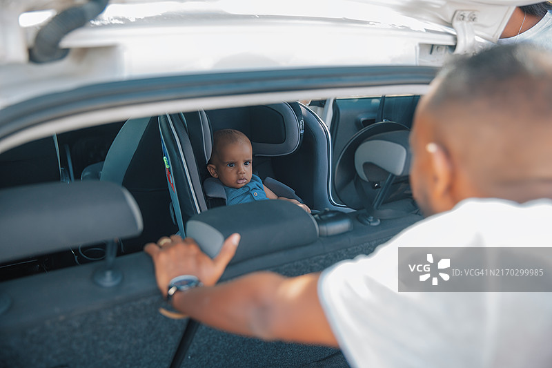 男人 наклонился в открытый багажник машины и смотрит на ребенка, сидящего в автокресле图片素材