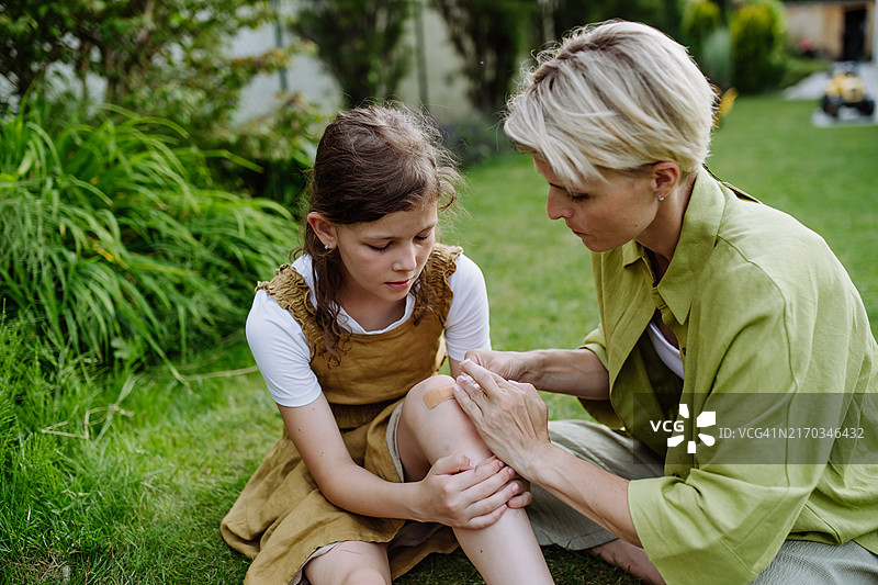 母亲处理女儿的伤口。摔倒后受伤、肘部流血。妈妈拿着创可贴安慰哭泣的女孩图片素材