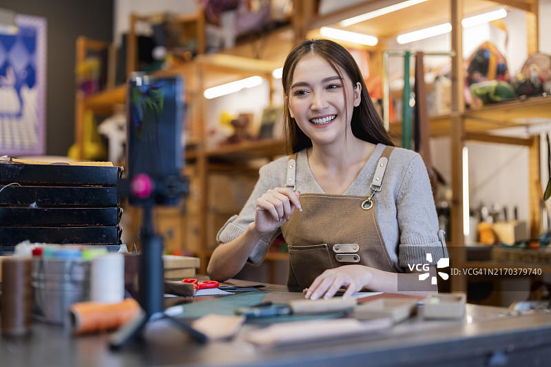 制作皮革包的在线课程，亚洲女性手工艺人网红在线教学如何制作皮革包，她正在通过智能手机直播与学生交谈图片素材
