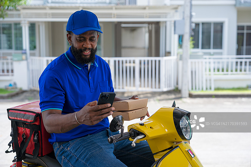 骑着踏板车送外卖的黑人男子，手持智能手机确认送货地点图片素材