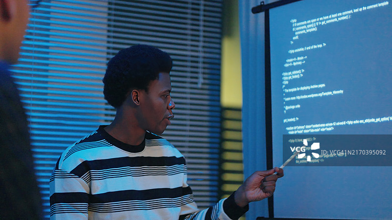 同事们在夜晚的会议室里看着投影屏幕，讨论计算机语言图片素材