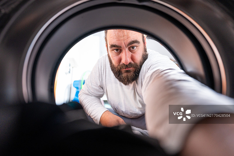 络腮胡男人伸手进前置式洗衣机图片素材