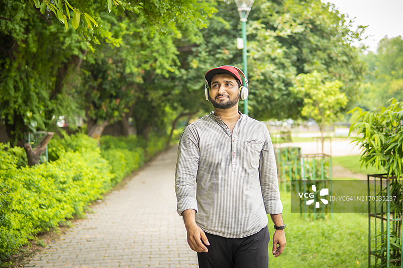 年轻男子在公园里散步，听着音乐，享受着新鲜空气。图片素材