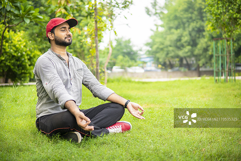 放松的年轻男子坐在绿草地上，在自然公园中进行冥想。图片素材