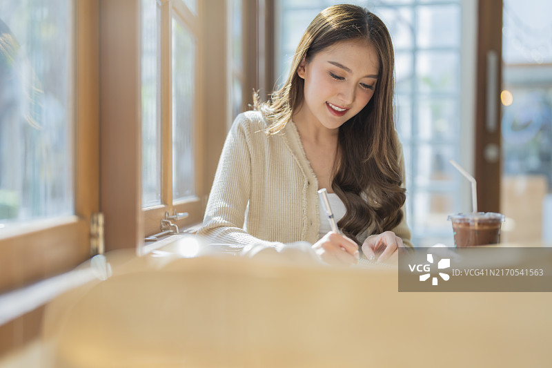 笑着的亚洲自由职业成年女性在咖啡馆写小说图片素材