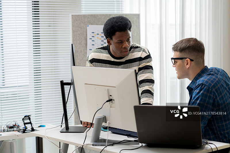 软件开发团队在现代软件开发办公室中进行实时协作，以编译源代码并解决错误，穿着商务服装和休闲服装，在带有笔记本电脑和电脑显示器的办公桌前工作图片素材