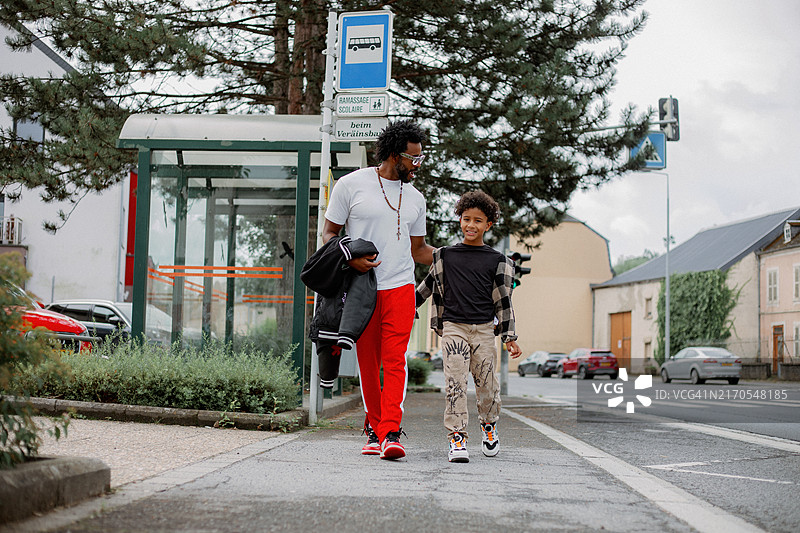 有爱的黑人父亲回头看着快乐的儿子，两人一同离开街边的公交车站。图片素材