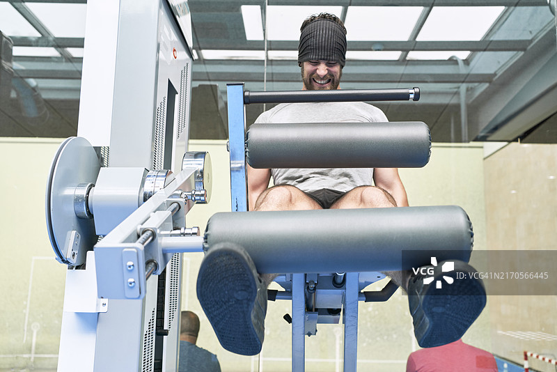 健身男人在健身房用器械努力锻炼腿部图片素材