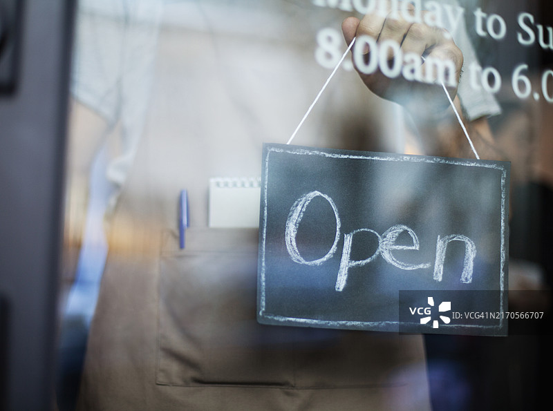 中年男人站在小型咖啡馆面包店餐厅的窗边，手持营业中标志图片素材