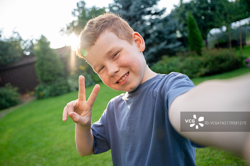在日落时分的后院自拍并做出和平手势的快乐红发男孩图片素材