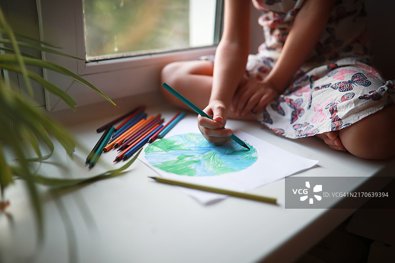 环境保护与创意：小女孩在窗台上用铅笔描绘地球图片素材