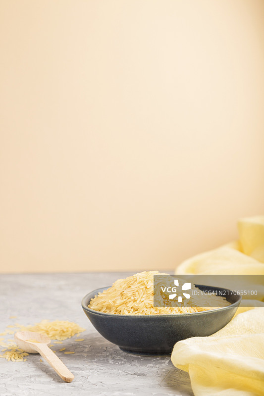 灰色和橙色背景上的蓝色陶瓷碗与金色生米和木勺图片素材