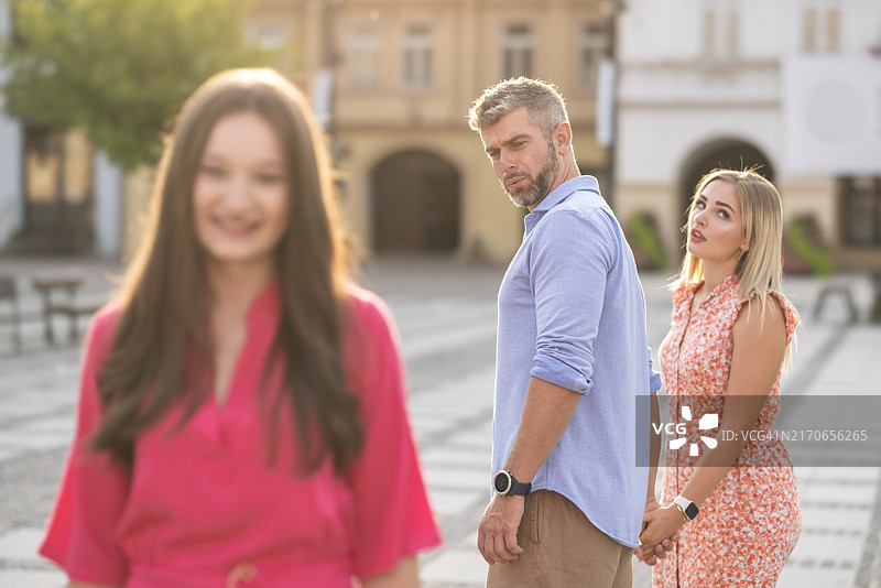不忠的花花公子：一个男人和女友走在街上，却转身欣赏另一个女人，女友对他很不满图片素材
