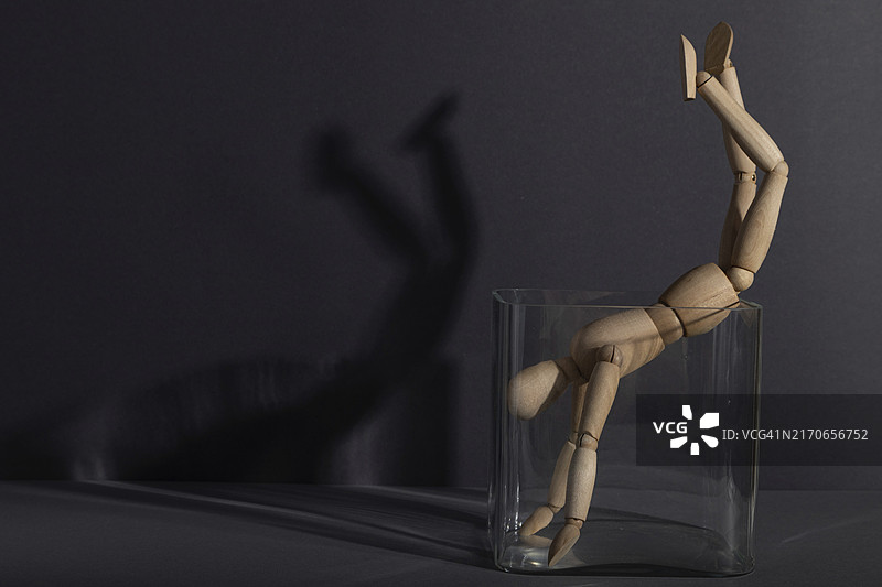灰色背景玻璃立方体中的木制人体模型：关于囚禁、打破规则、孤独和抑郁症图片素材