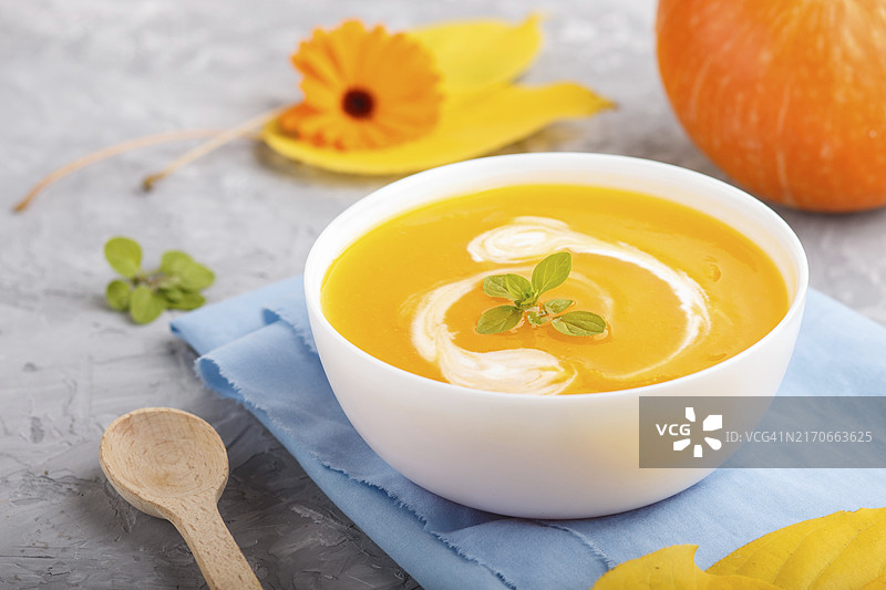 灰色背景中白色碗里的传统南瓜奶油汤，配蓝色餐巾图片素材