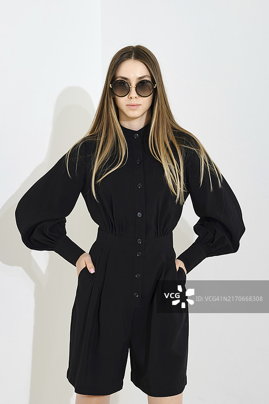 年轻女子身穿黑色短裙和宽松袖衬衫，在白色背景前摆姿势图片素材