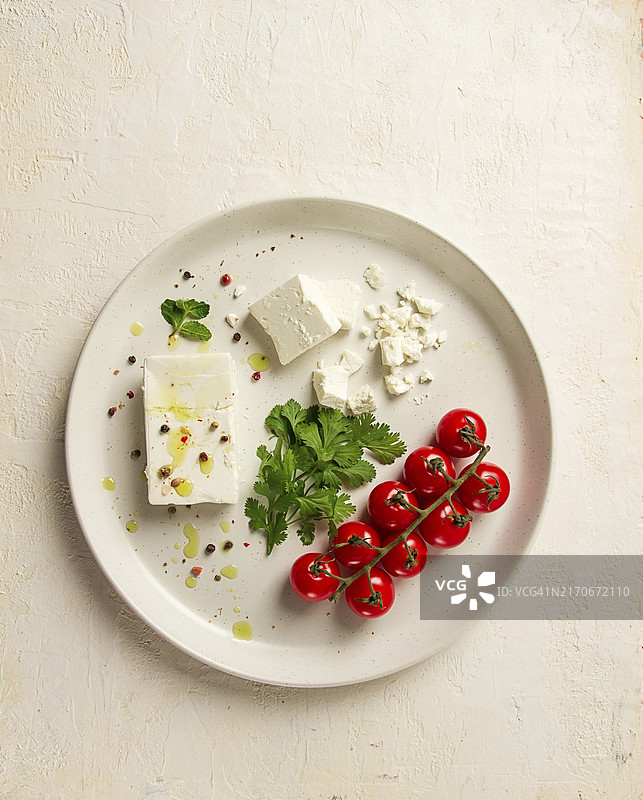白色盘子里的菲达奶酪、圣女果、绿色黄油和蔬菜沙拉，开胃菜，顶部视图，特写图片素材