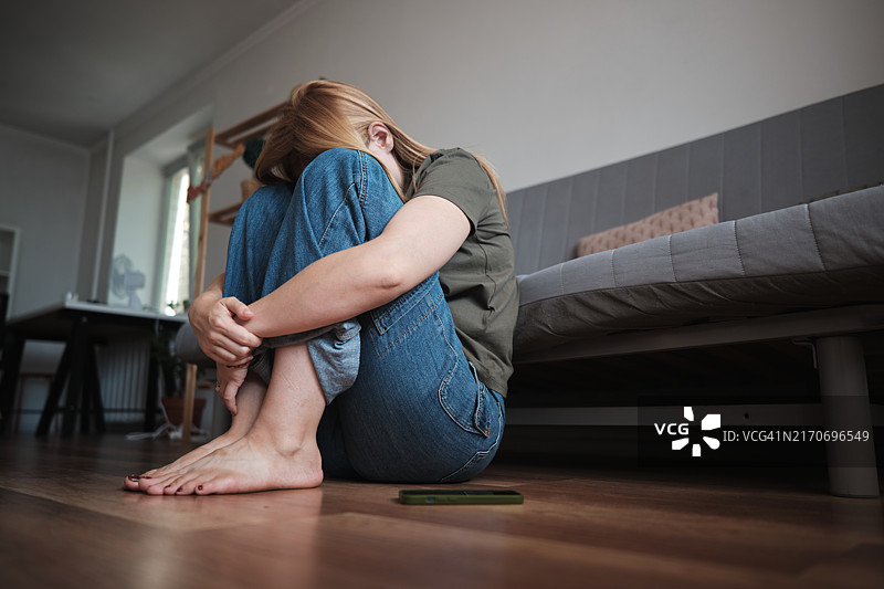 网络欺凌。沮丧的少女坐在地板上，抱着膝盖哭泣图片素材