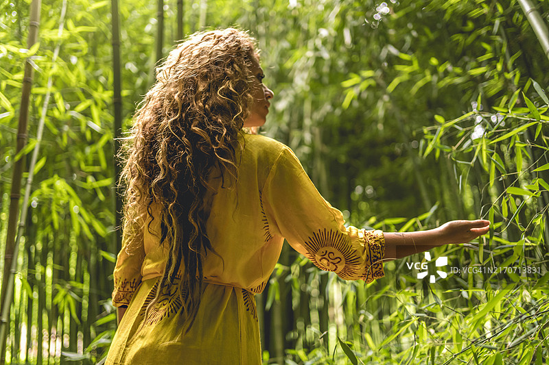 穿着亮黄色连衣裙的女人站在茂密的竹林中图片素材