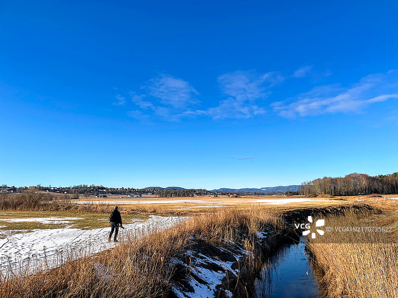 早春时节，沿着小溪寻找鸟类的男人，天气晴朗，天空蔚蓝。图片素材